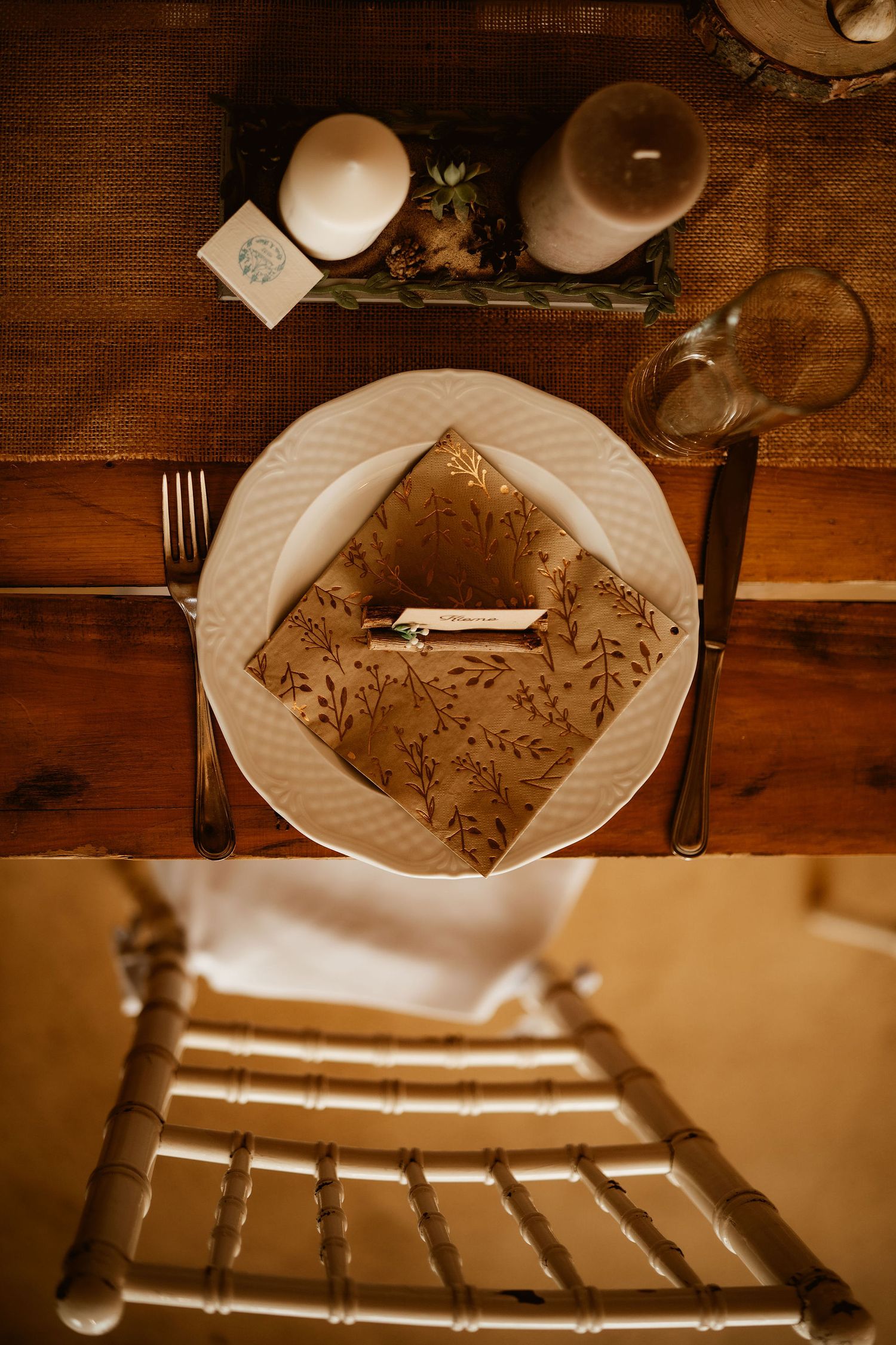 Elegant table setting with white plate, floral napkin, and candles on wooden surface.