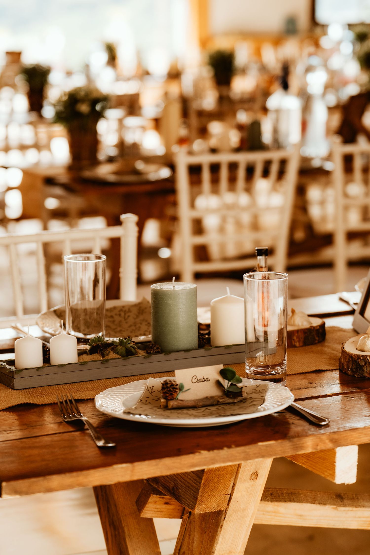 Rustic wedding table setting with candles, wood slices, and white place settings.