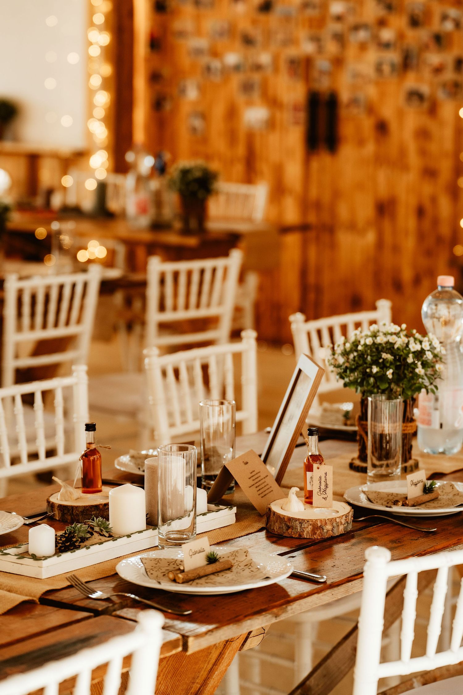 Rustic wedding reception table with white chairs, candles, and floral centerpieces.