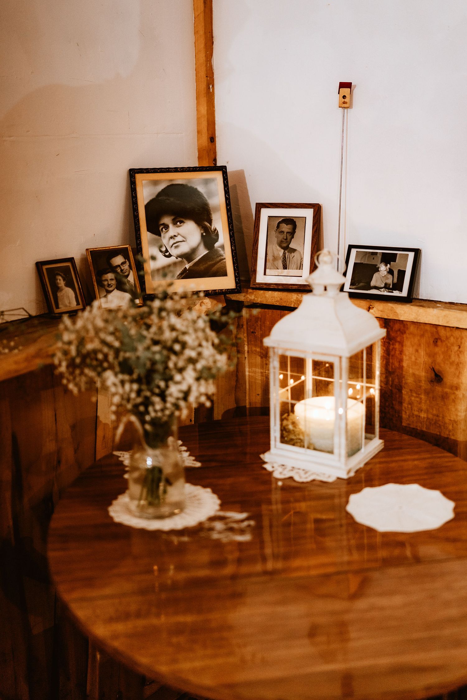 Vintage photographs and a white lantern displayed on a wooden table with dried flowers.