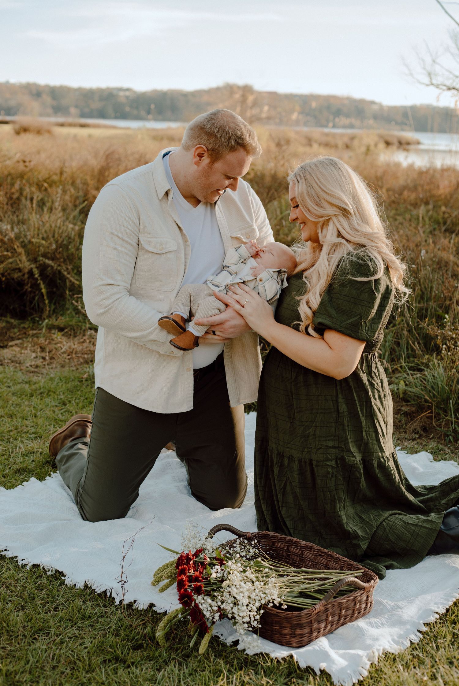 A couple having a picnic on a blanket with a basket and flowers in an outdoor setting at sunset.