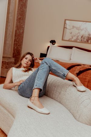 Woman relaxing on grey couch wearing vintage jeans and white flats in warm lighting.