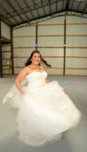 A person in a flowing white wedding dress twirls and dances in an open venue.