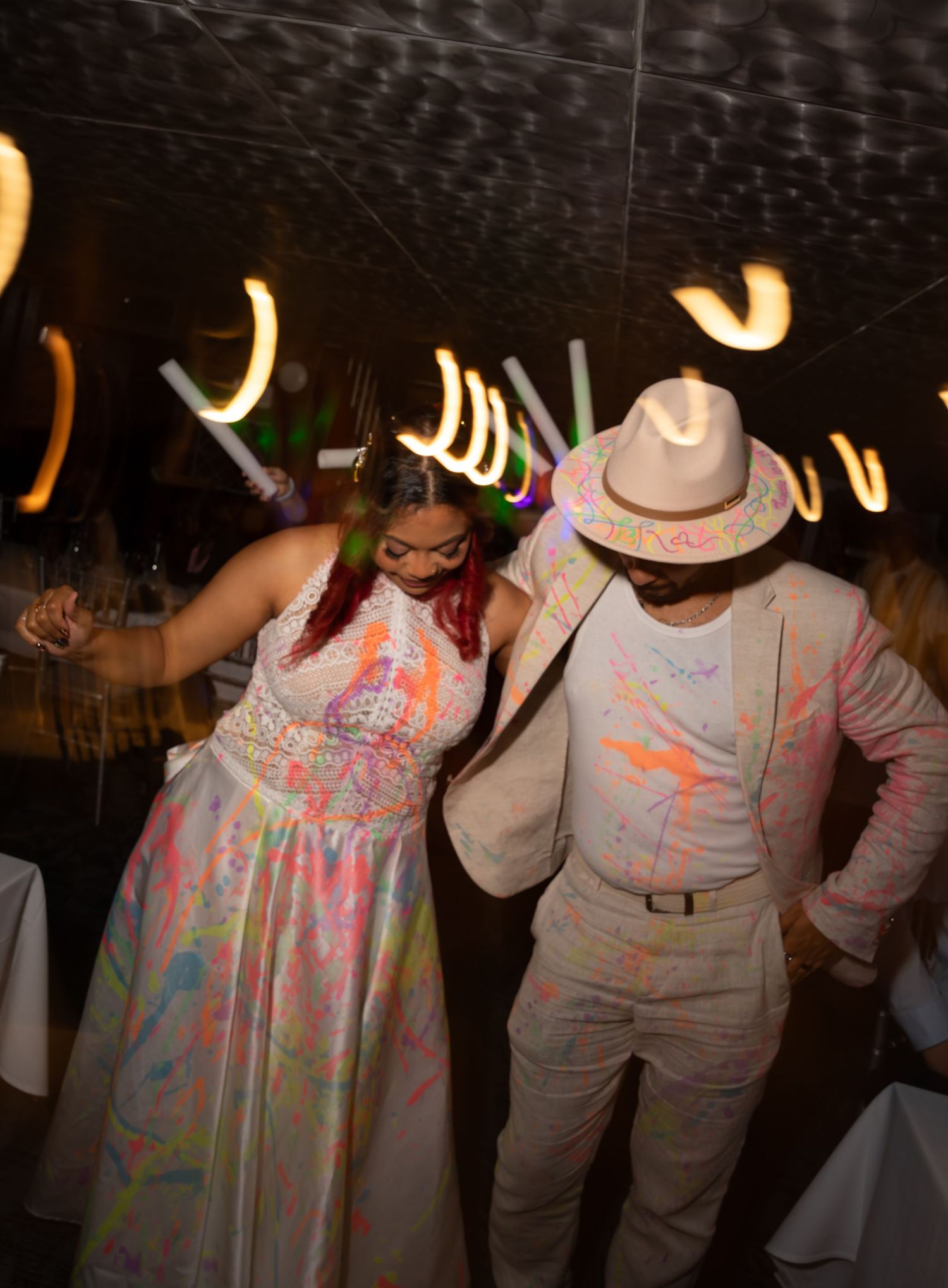 Wedding guests dance in colorful attire under party lights during reception.