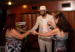 People dancing and mingling at a party in a wood-paneled venue with warm lighting.