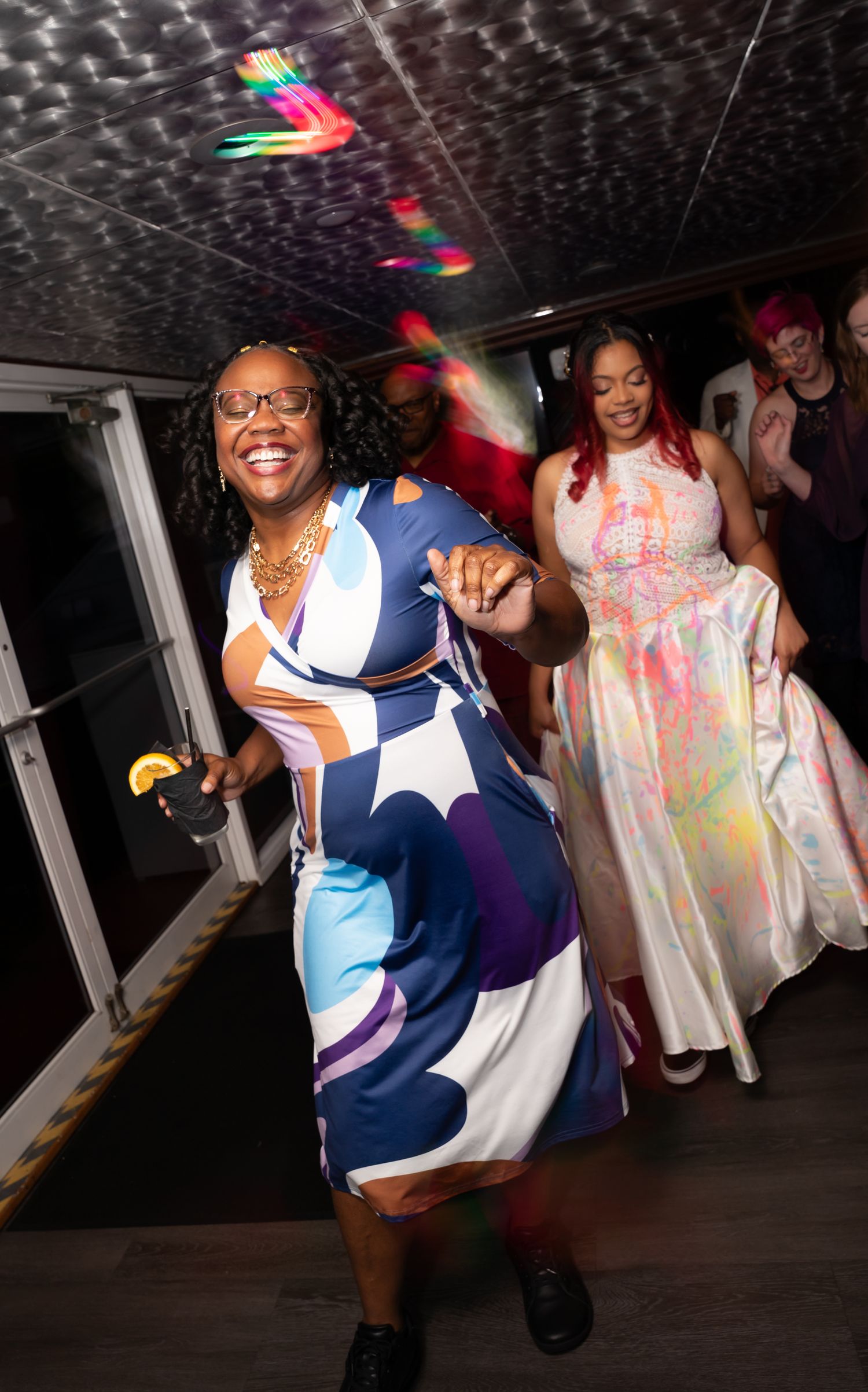 Wedding guests dancing energetically in colorful dresses under party lights.