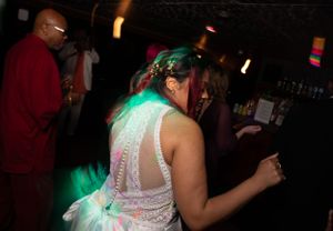 Bride dances in white lace dress under green party lights at wedding reception.