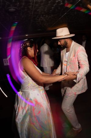 Dance partners covered in colorful paint embrace on a dimly lit dance floor.