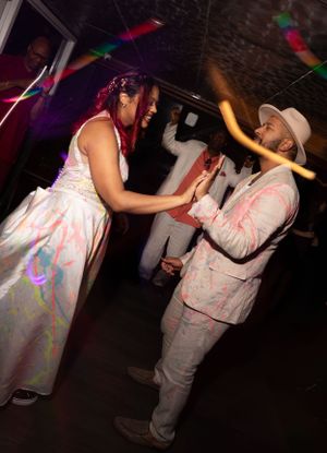 People dancing in white and pink outfits under colorful club lighting.