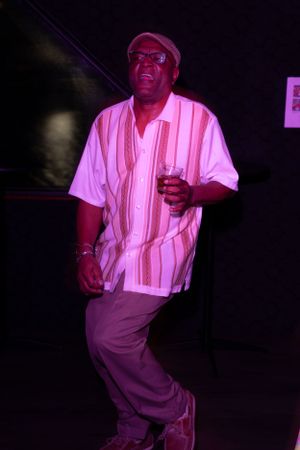 Person in striped shirt dancing under purple stage lighting at a nightclub.