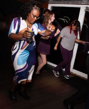 Dancers move energetically in a dimly lit room during what appears to be a social dance event.