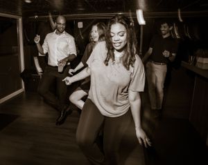 Dancers move energetically across a dark dance floor at a celebration.