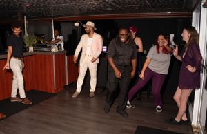 Group of people dancing together in a dark room with spotlights casting shadows.
