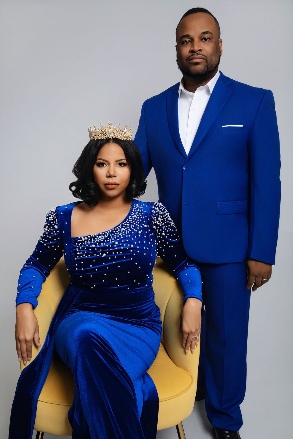Formal portrait with couple in coordinating royal blue outfits against grey backdrop.