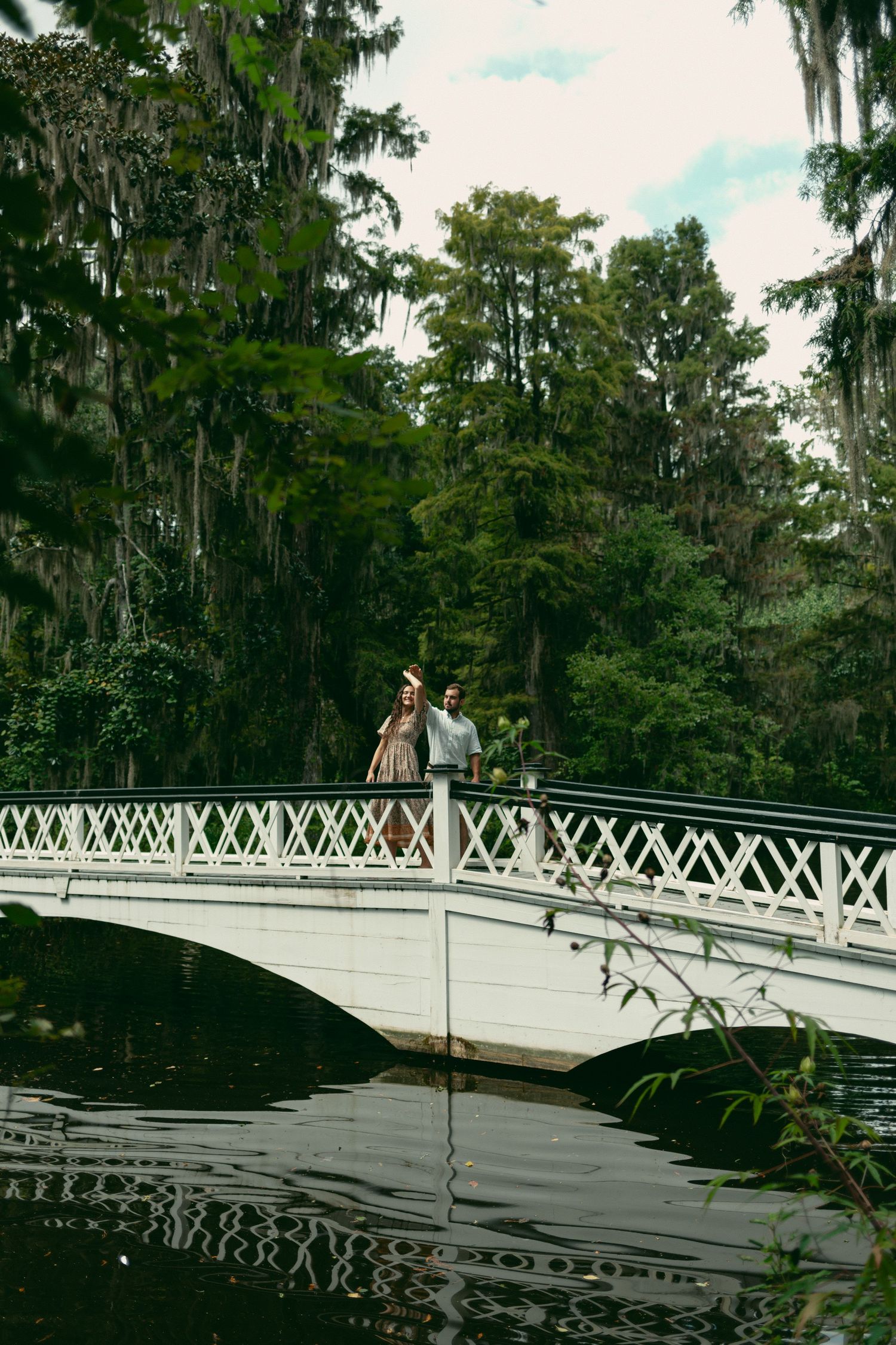 A couple embraces on a white arched bridge reflecting in dark waters below.