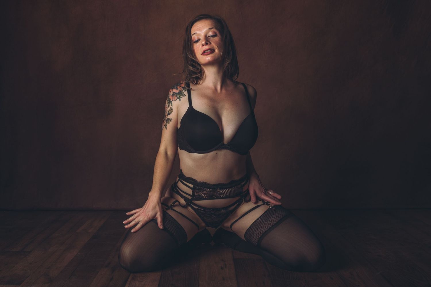 Artistic boudoir photograph featuring tattooed figure in black lingerie set on wooden floor. bridal boudoir