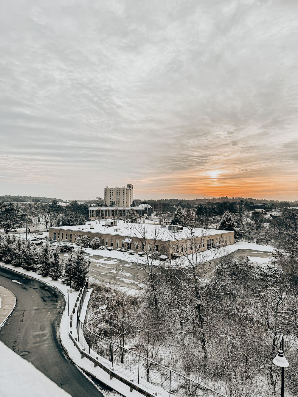 Aerial view of a snow-covered town at sunset with winding roads and historic buildings against an orange winter sky.