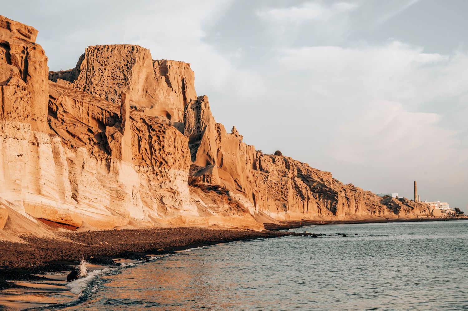 Orange coastal cliffs towering over ocean shoreline at sunset.