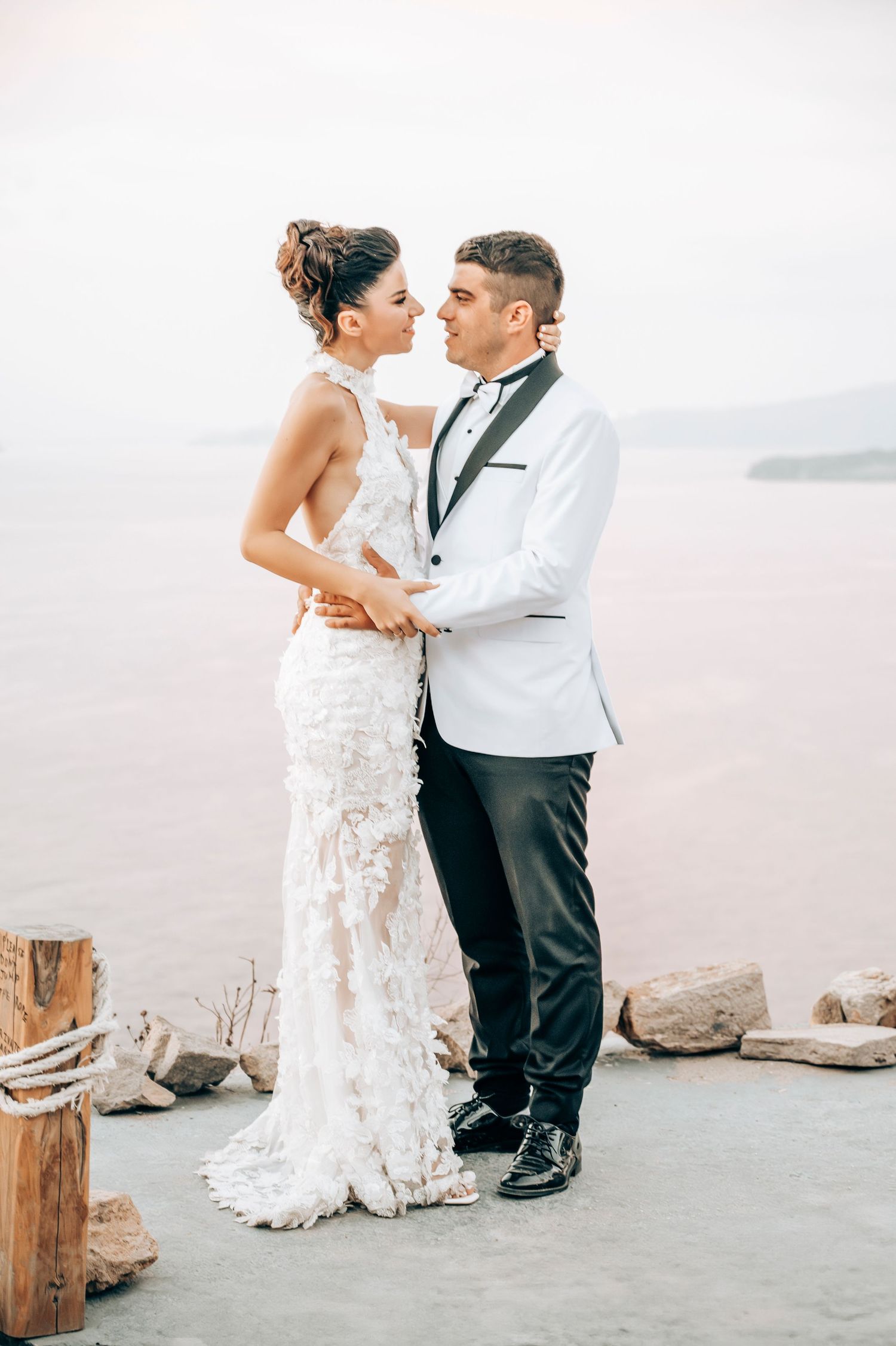 A romantic wedding couple embraces on a seaside terrace in formal attire.