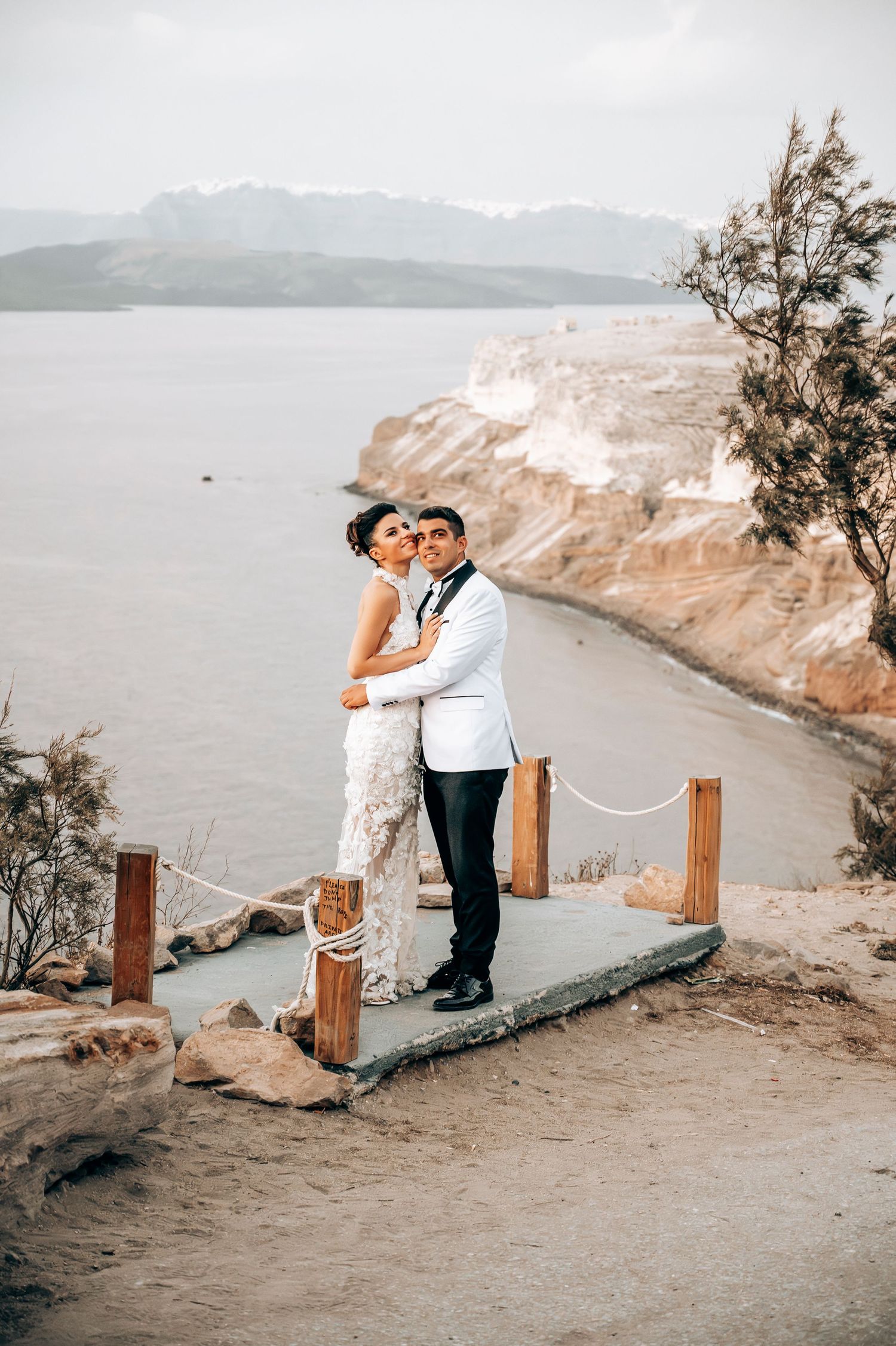 Newlyweds share an intimate moment on a scenic clifftop overlooking the ocean.