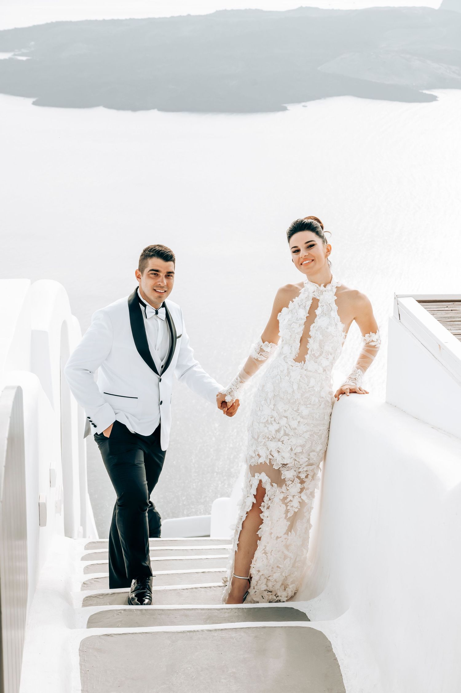 Elegant couple walking down traditional white Santorini staircase during wedding photoshoot.