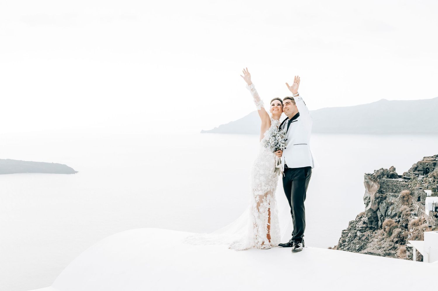Celebratory wedding pose against stunning Santorini caldera view.