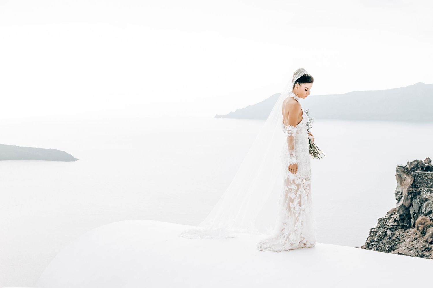 Ethereal bridal portrait on white rooftop overlooking Aegean Sea.