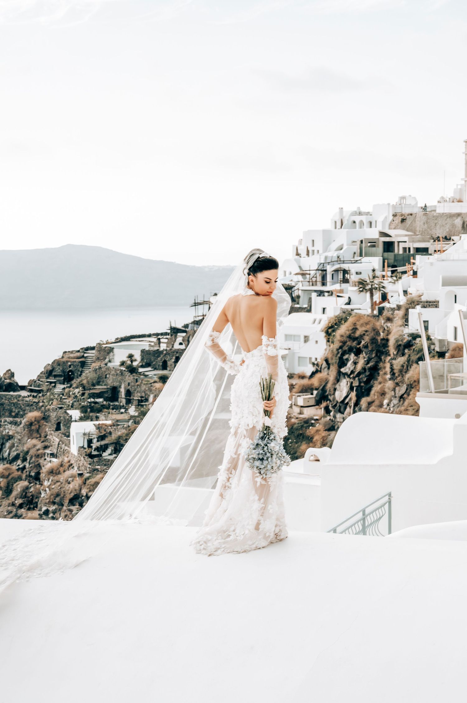 Romantic bridal portrait on Santorini steps with flowing veil and Mediterranean vista.