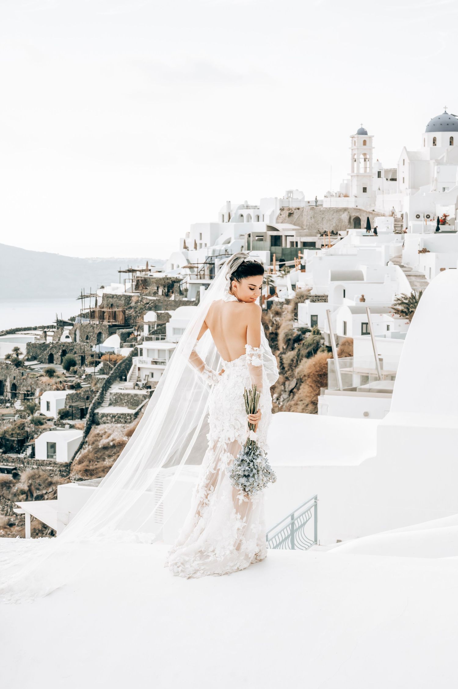 A wedding dress flows in the wind against the iconic white architecture of Santorini, Greece.