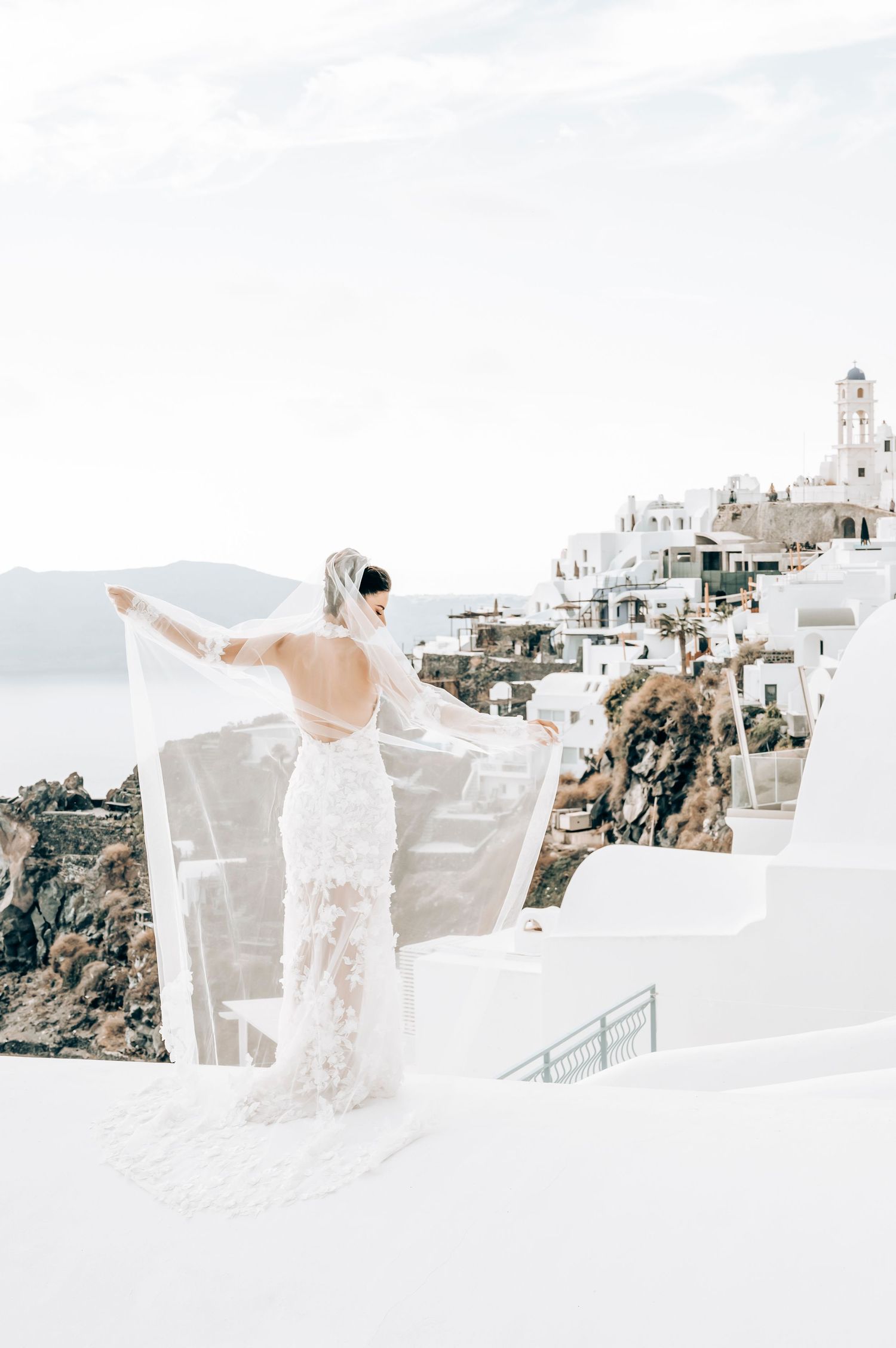 Ethereal bridal portrait with flowing veil against the backdrop of Santorini's white buildings.
