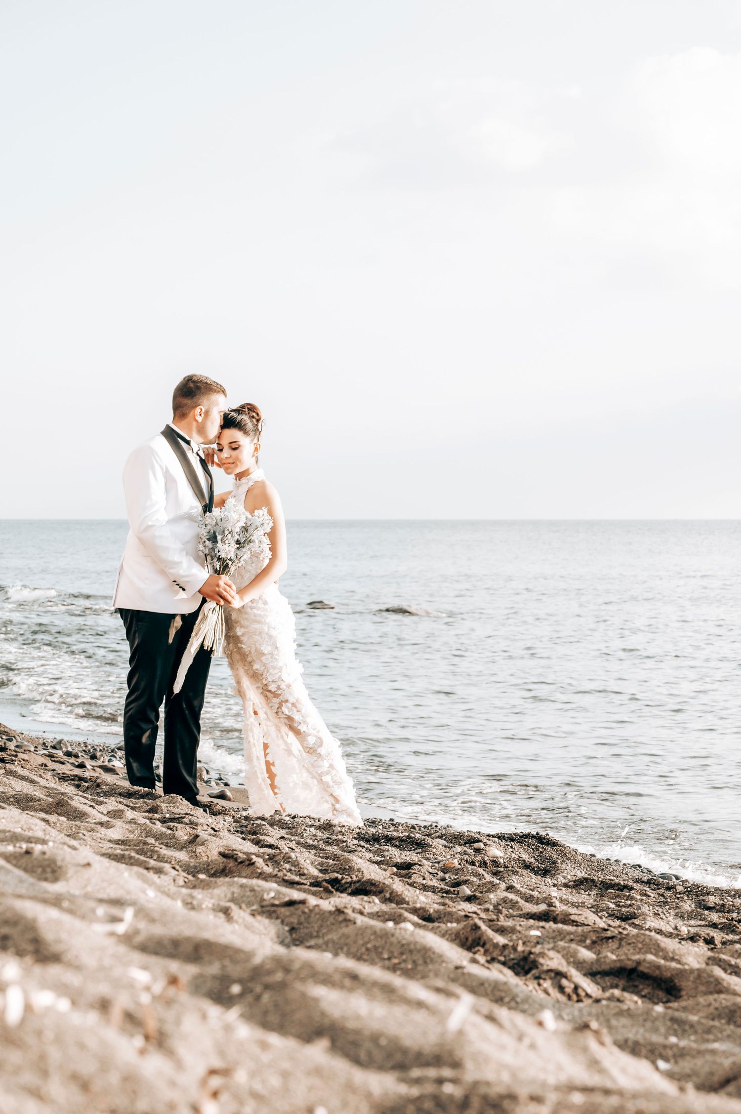 A romantic beach wedding portrait with couple standing by the Mediterranean Sea.