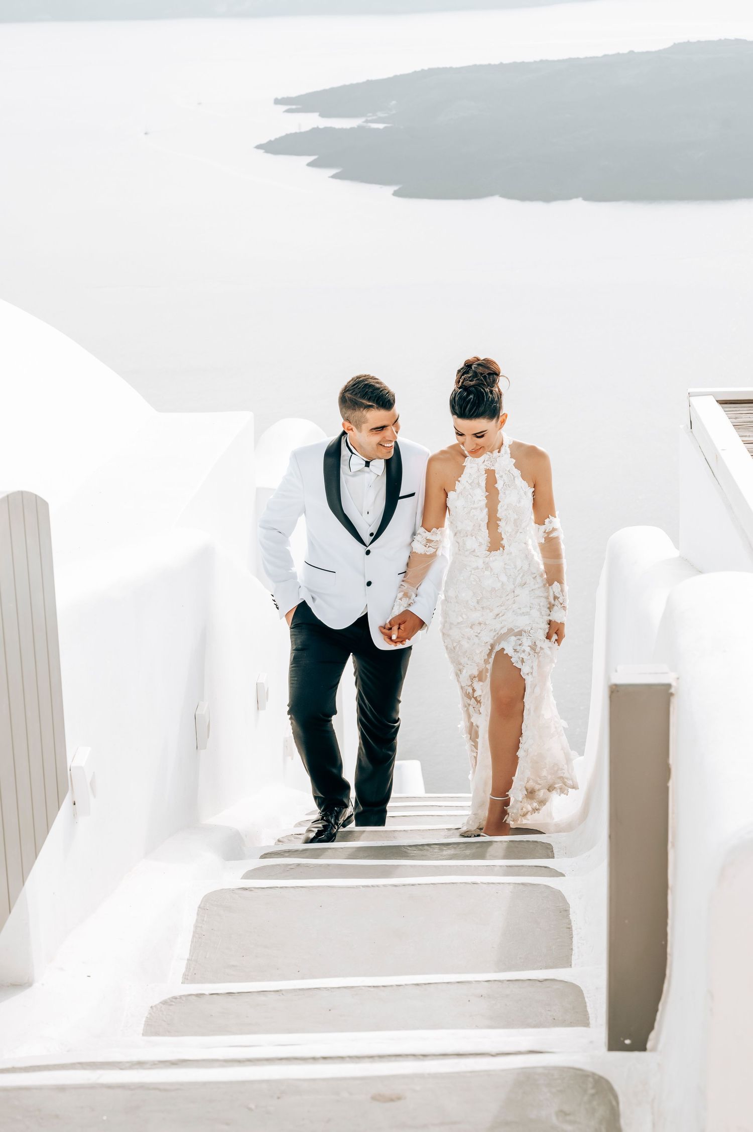 Wedding couple descending white stairs together in Santorini, Greece.