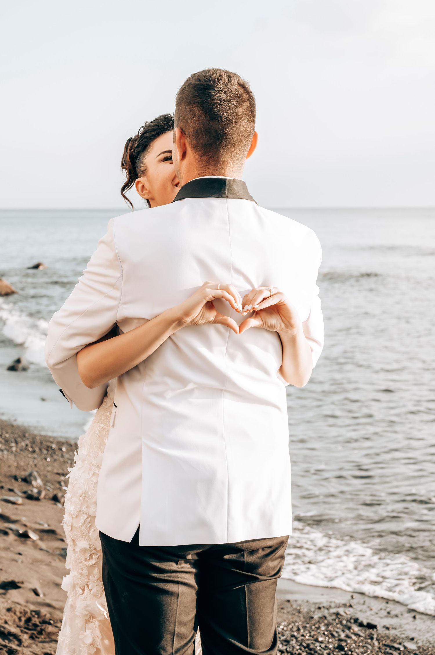 Intimate wedding moment captured on a beach with hands forming heart shape.