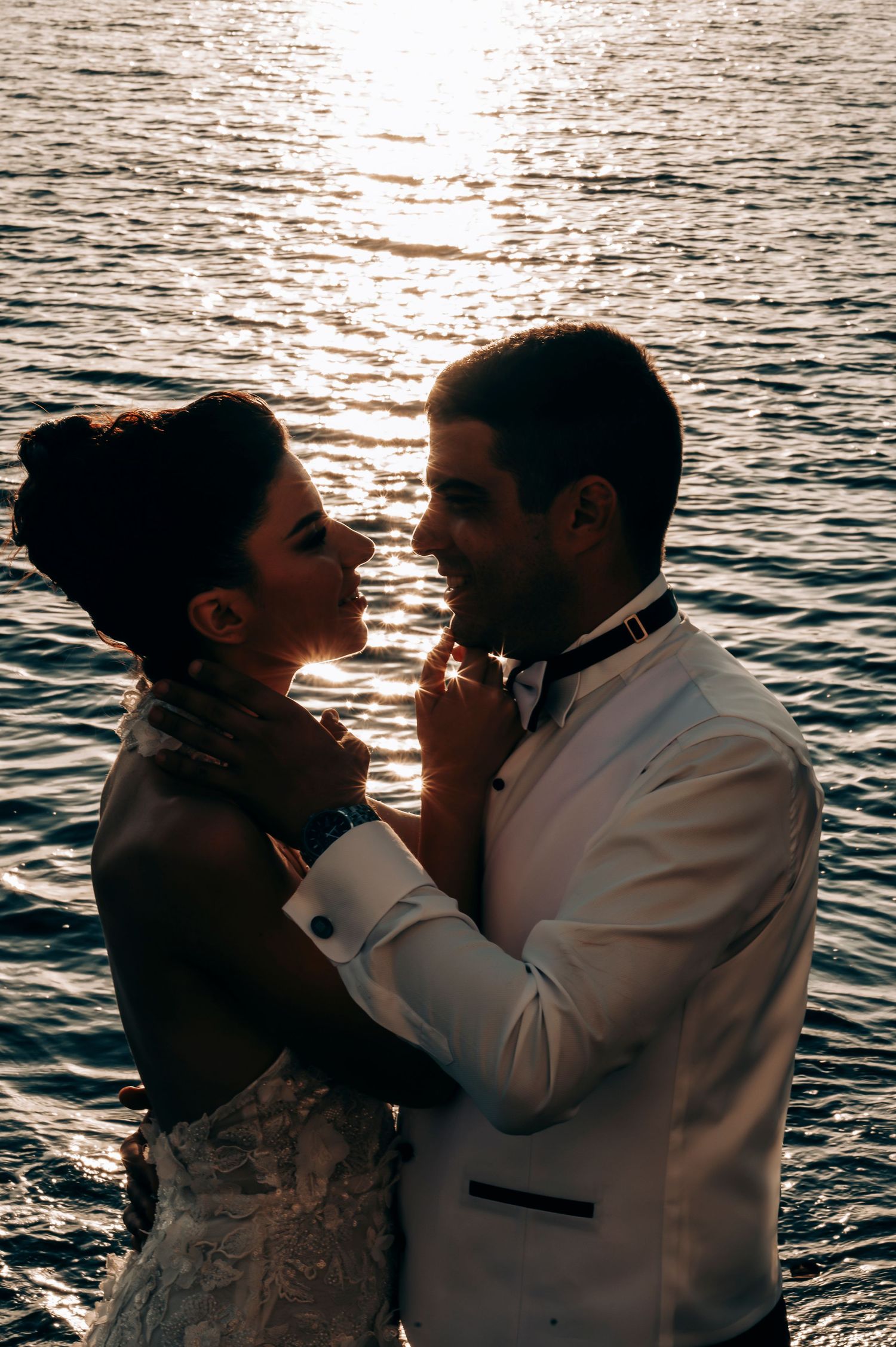 Romantic sunset silhouette of newlyweds embracing by the sparkling ocean.