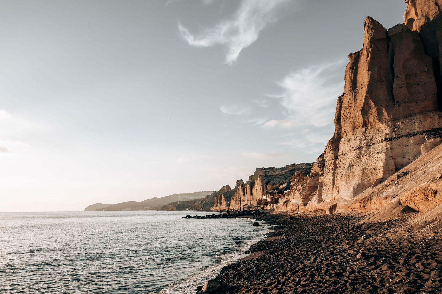 Dramatic coastal cliffs rising above rocky beach at sunset.