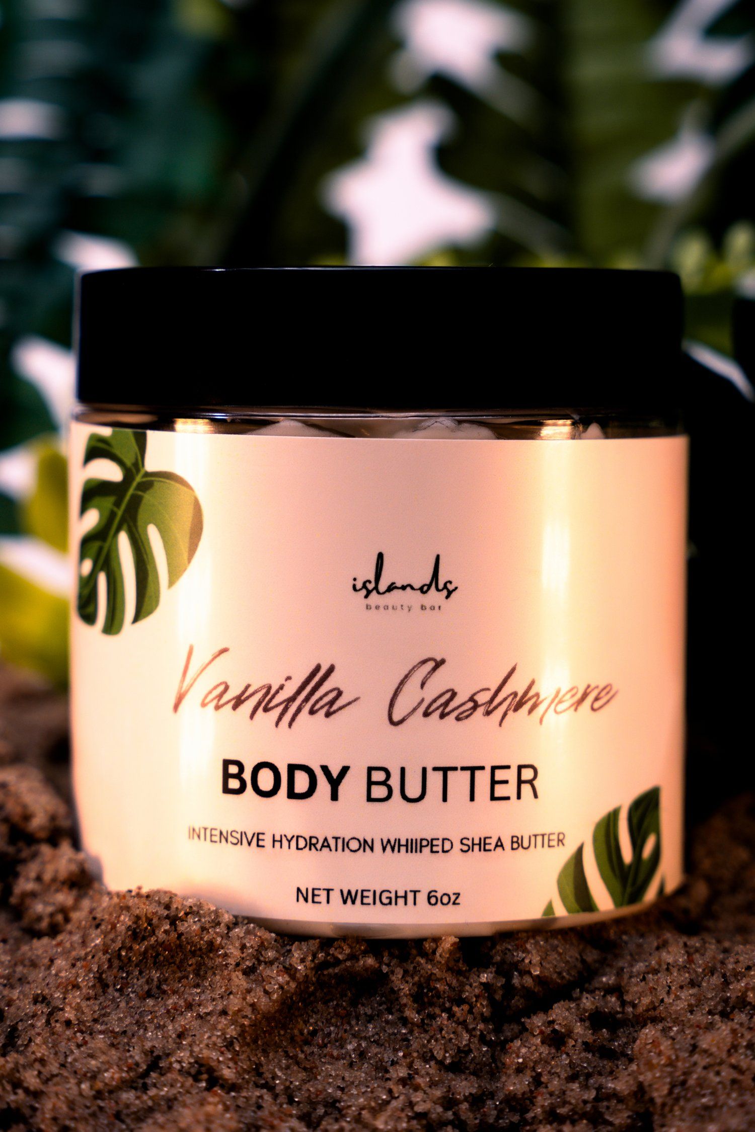 Vanilla Cashmere body butter jar with tropical leaves and warm lighting on soil background.