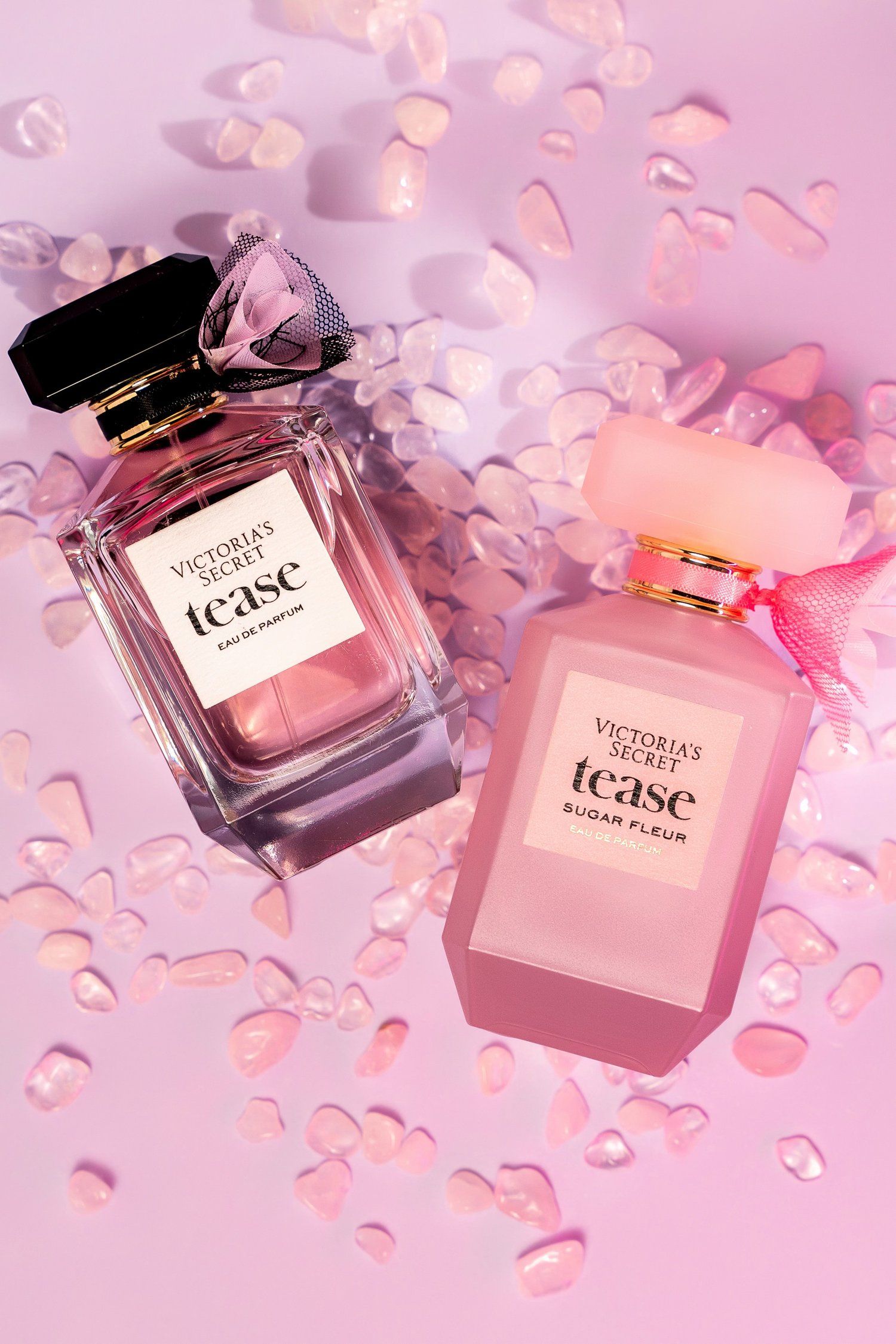 Victoria's Secret Tease perfume bottles on pink background with scattered rose petals.