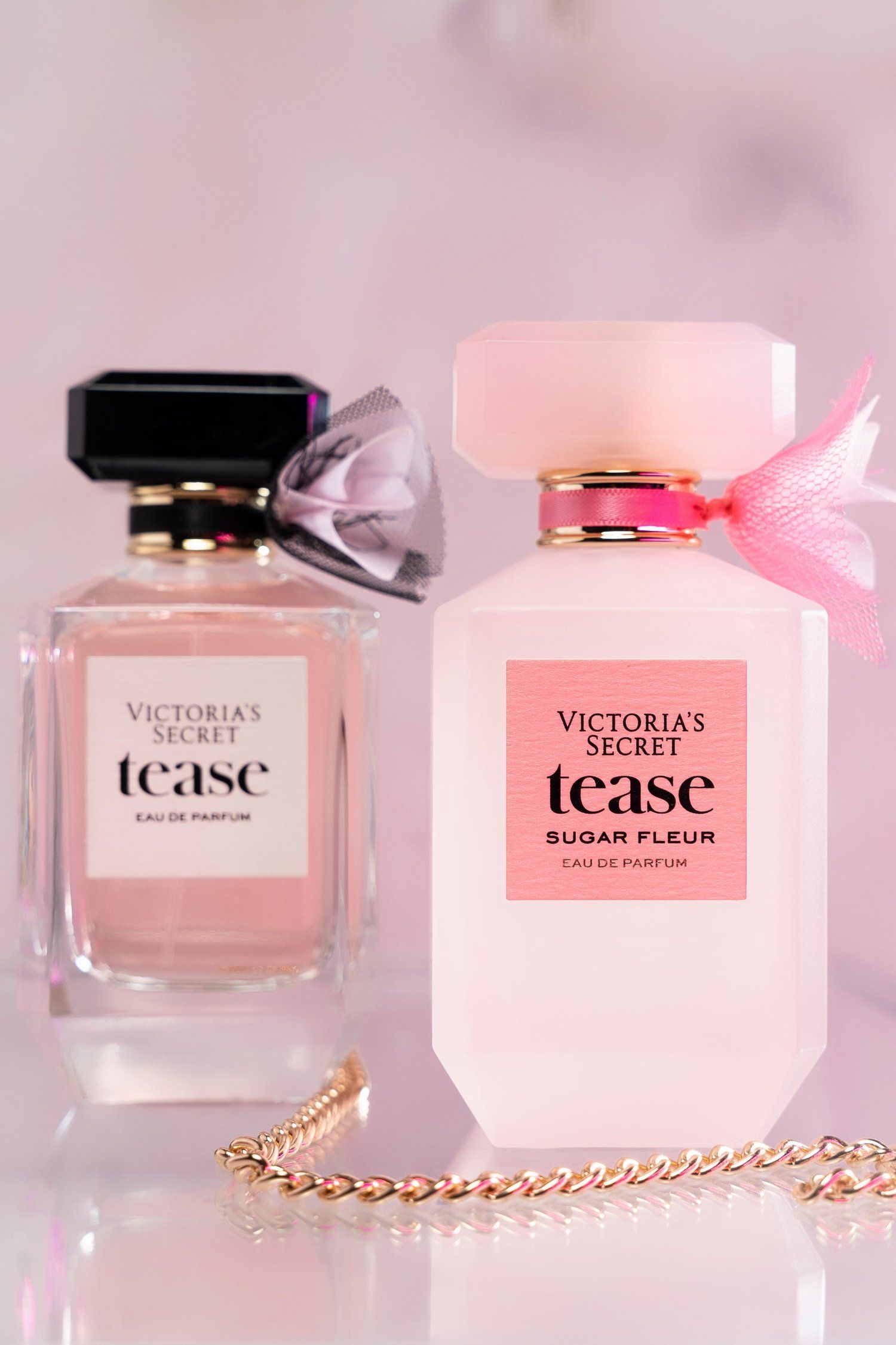 Two Victoria's Secret Tease perfume bottles with decorative chain and ribbon accents.
