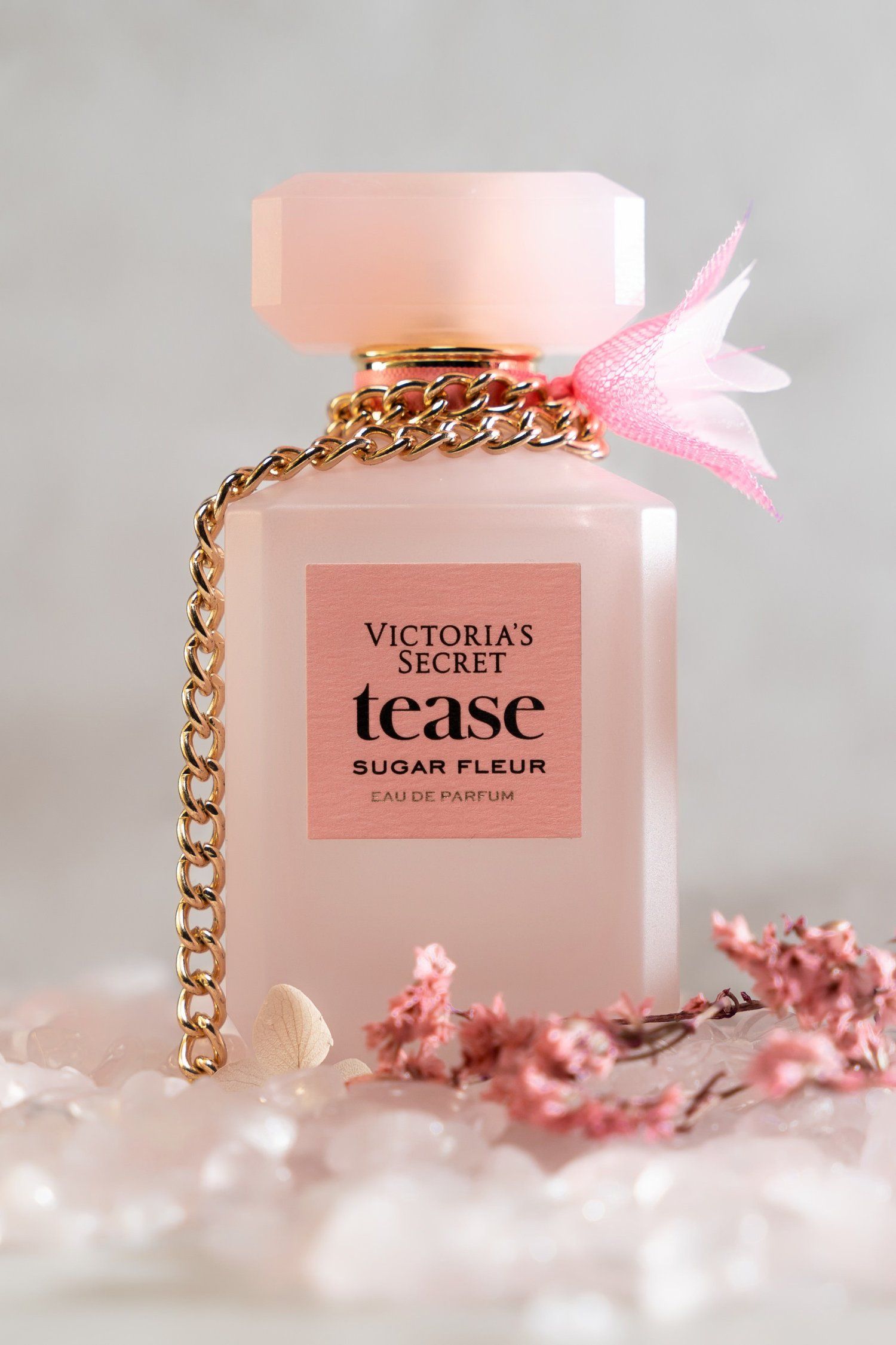 Victoria's Secret Tease Sugar Fleur perfume bottle with gold chain and pink floral elements.