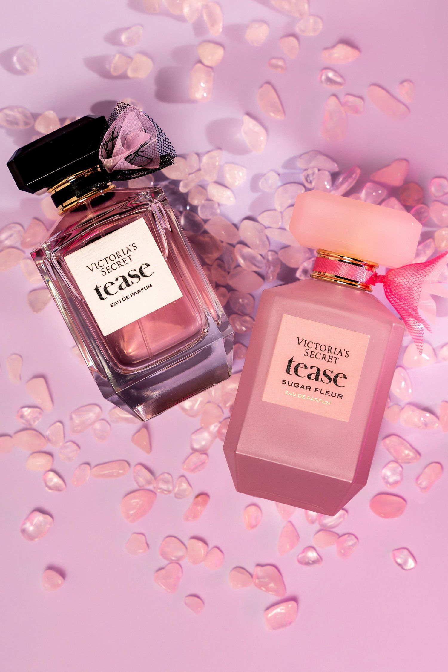 Victoria's Secret Tease perfume bottles arranged on pink background with scattered rose petals.