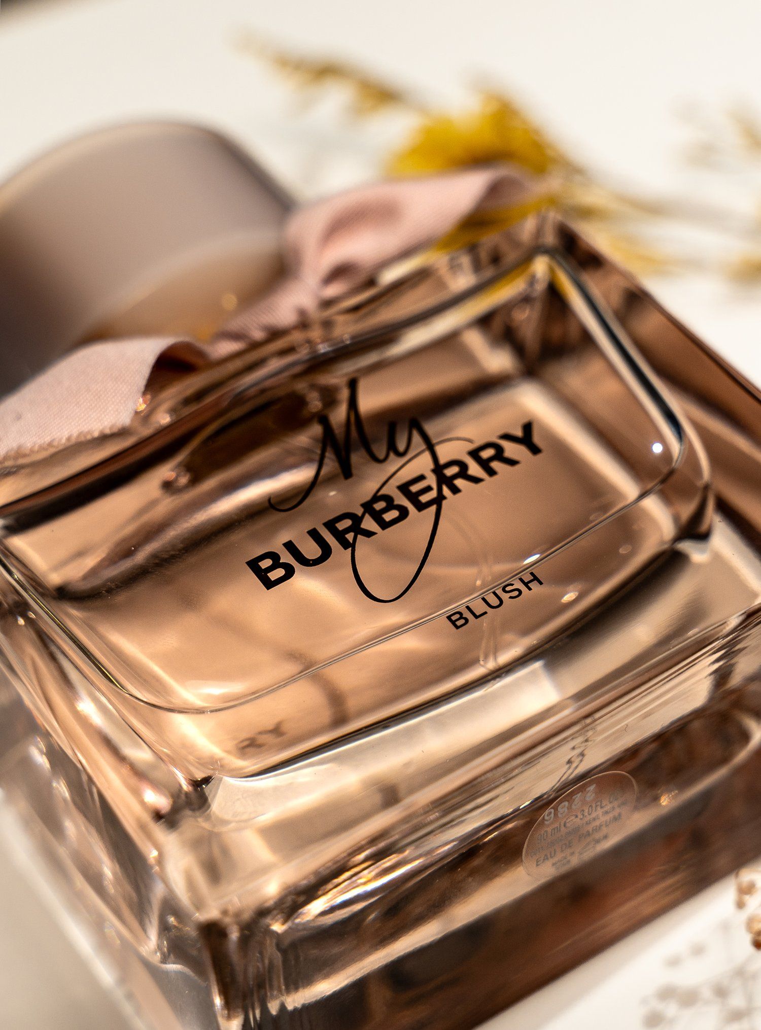 Close up of My Burberry Blush perfume bottle with golden cap and floral accents.