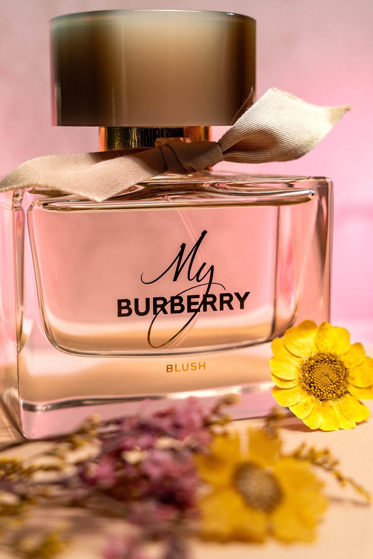 My Burberry Blush perfume bottle with yellow flower accent against pink background.