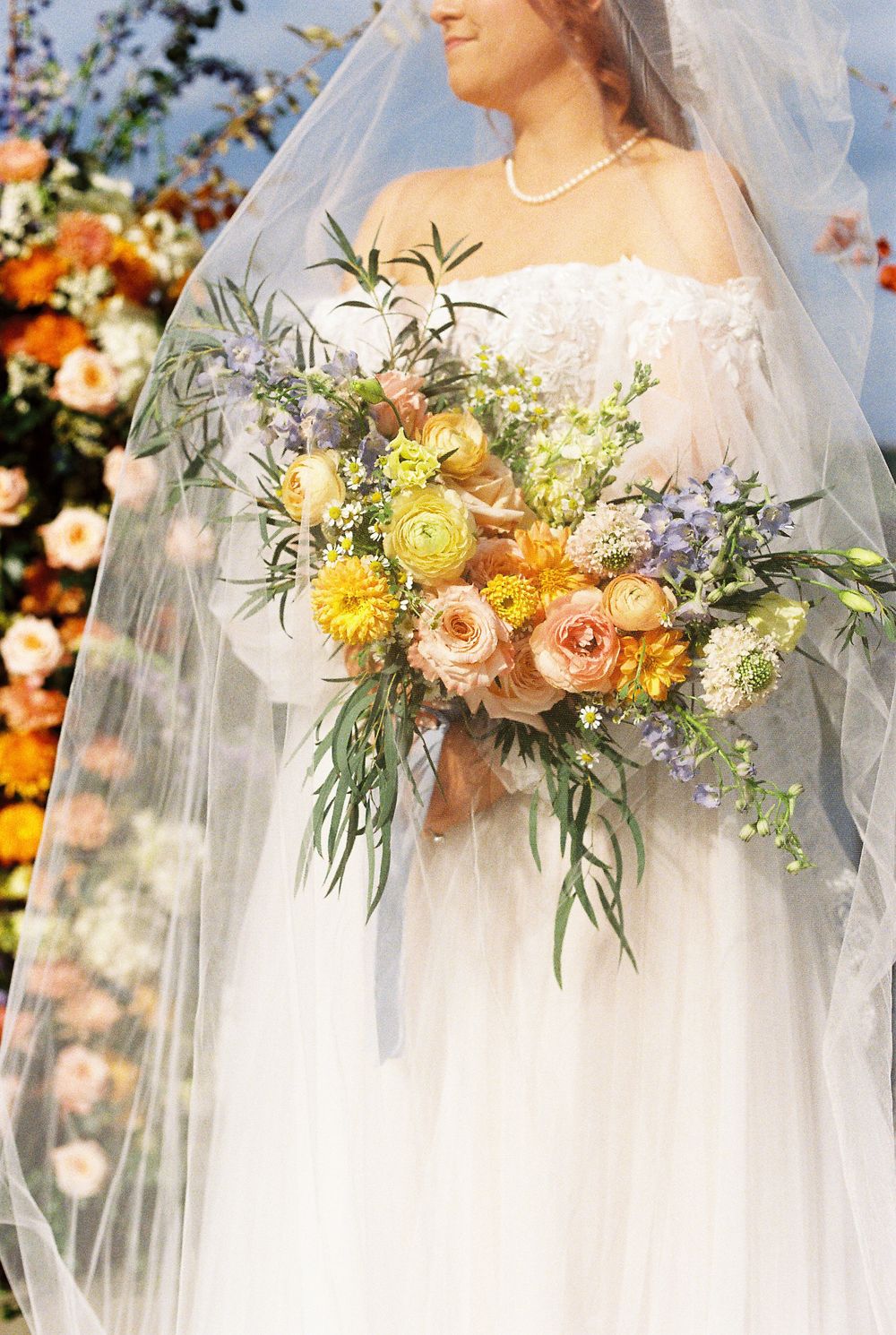 Close-up shots of a bridal bouquet with yellow, peach and lavender flowers against a white wedding dress.