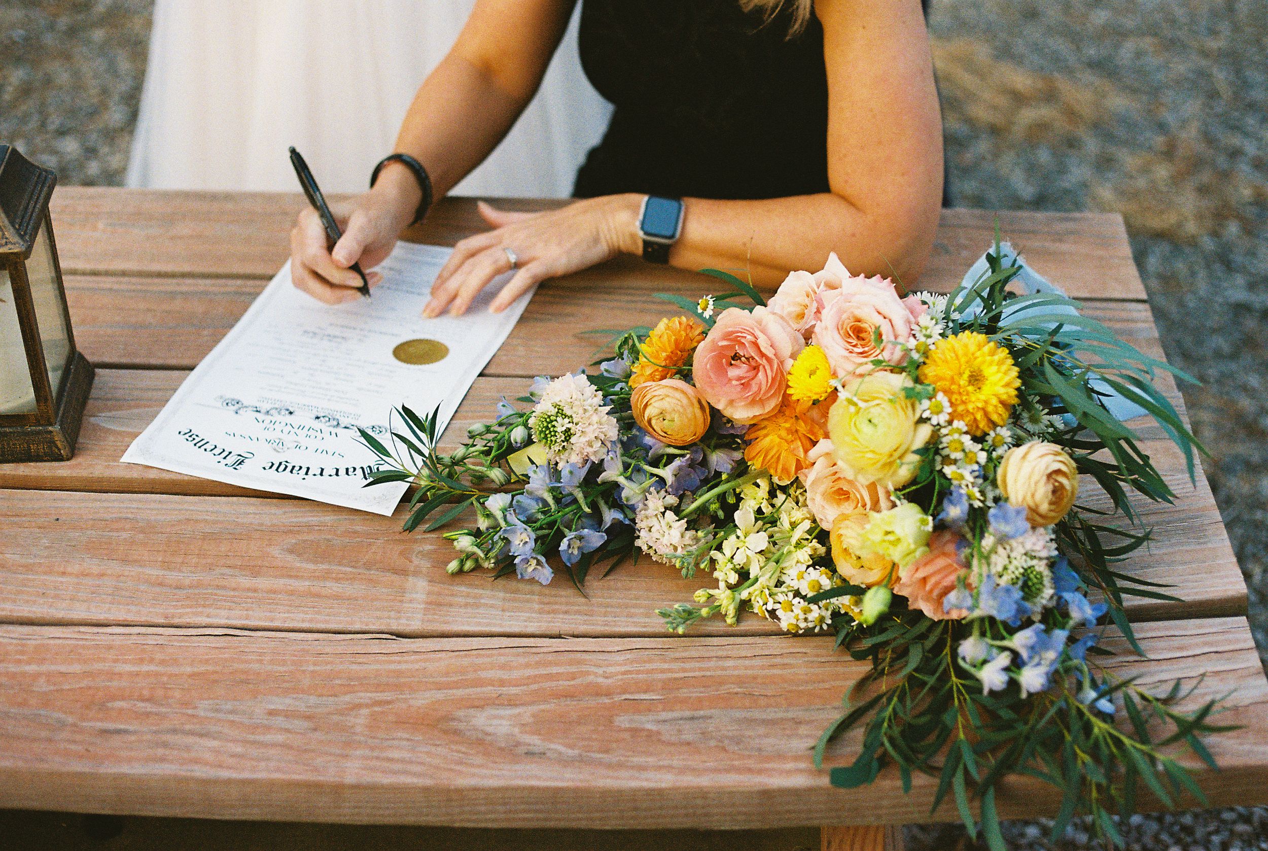 Wedding detail shot of signing documents with colorful floral bouquet on wooden table.