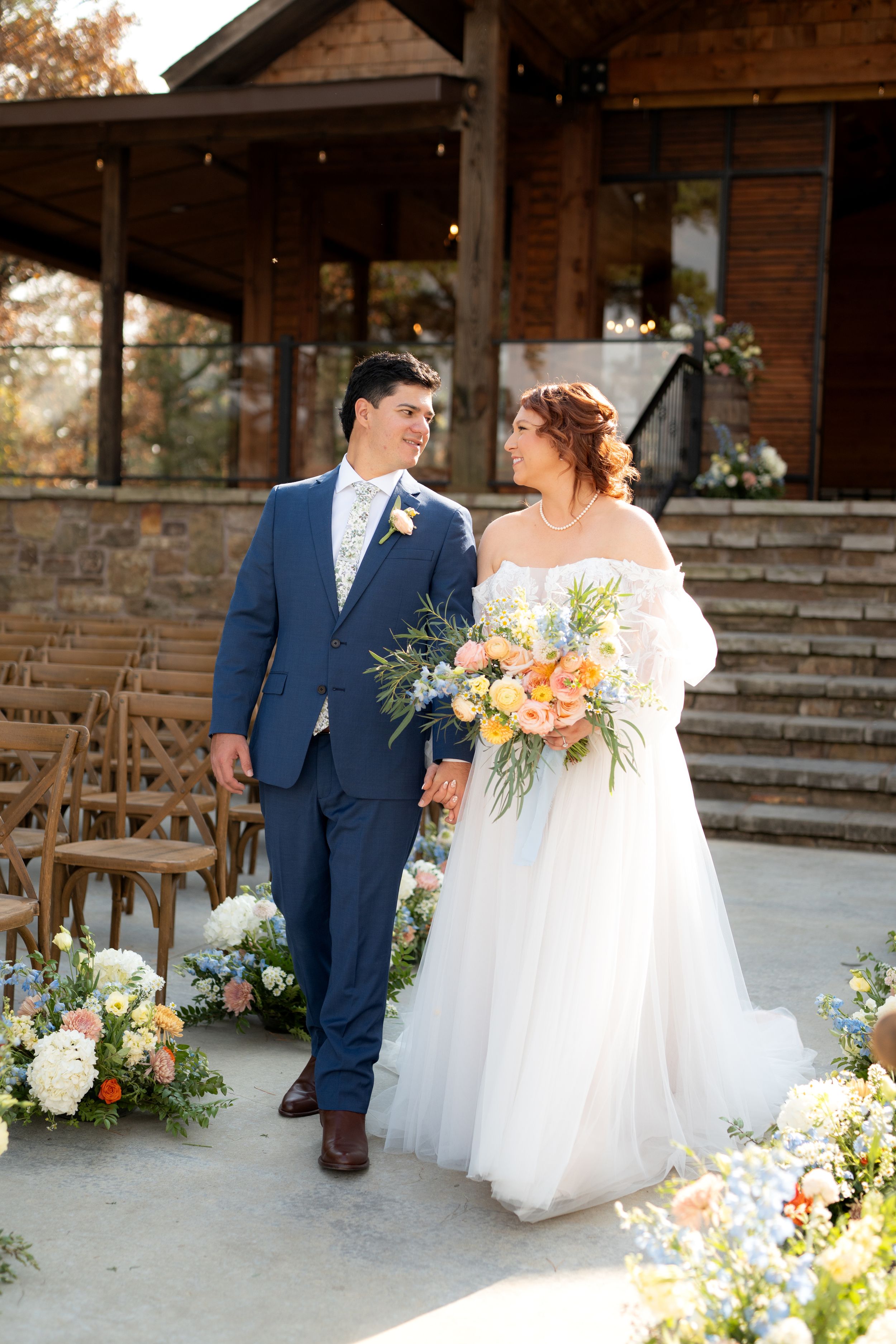 Wedding couple poses at rustic wooden venue with colorful floral arrangements and peach accents.