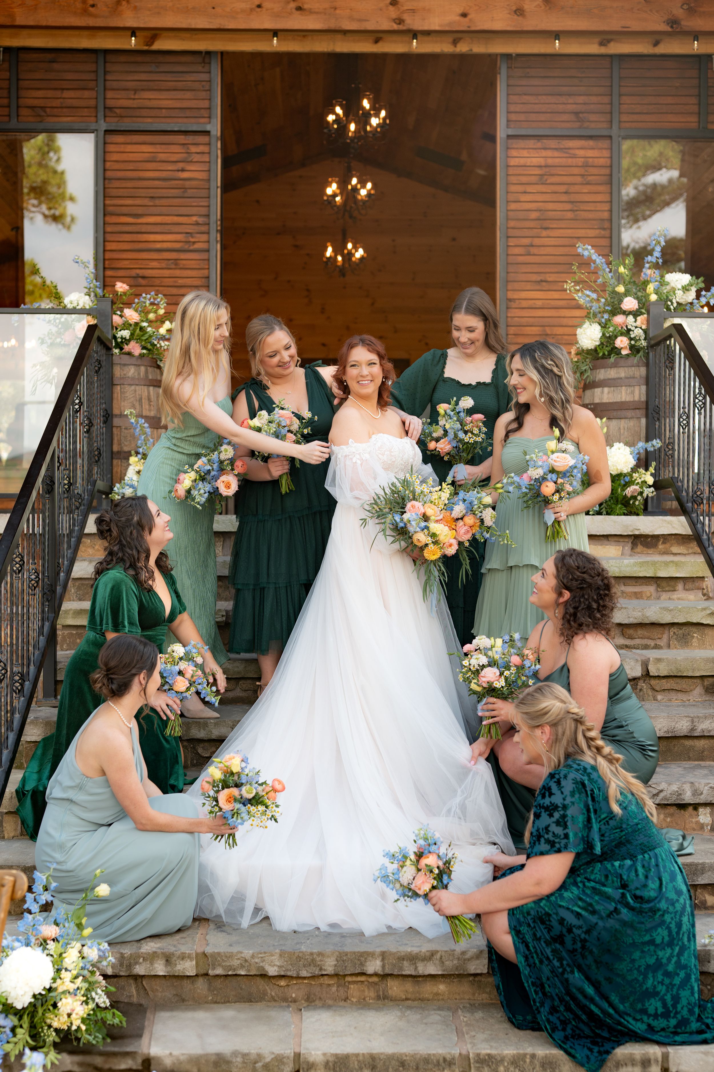 Wedding party in emerald green dresses gathered on rustic brick steps sharing a fun candid moment.