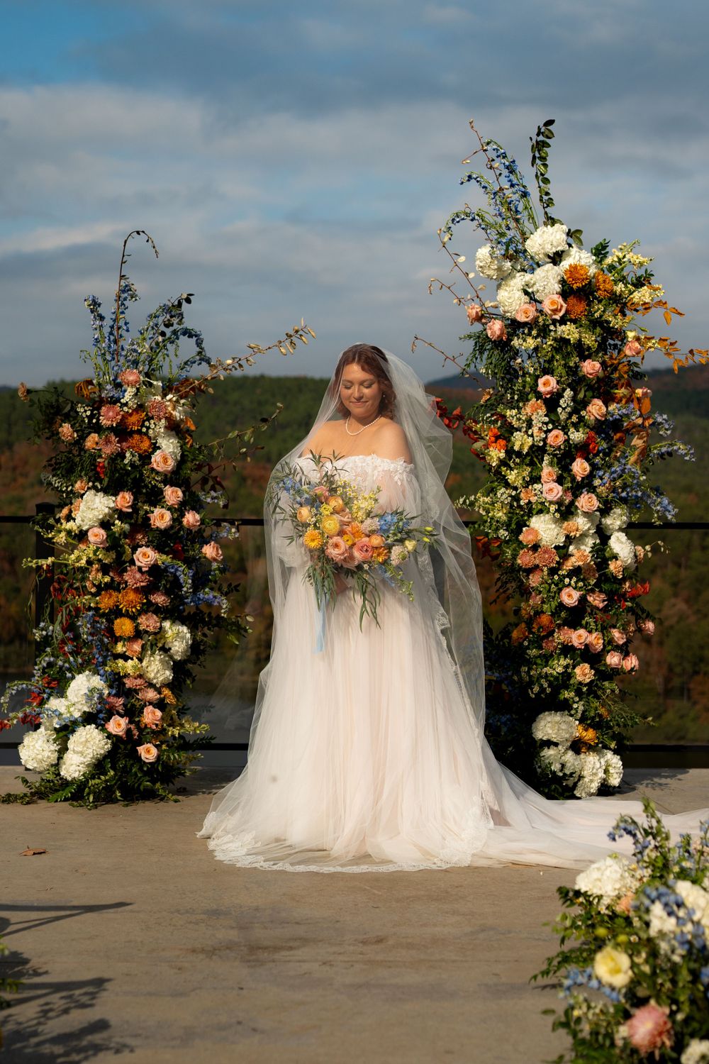 Stunning floral wedding arch with peach and white flowers against a cloudy mountain backdrop.