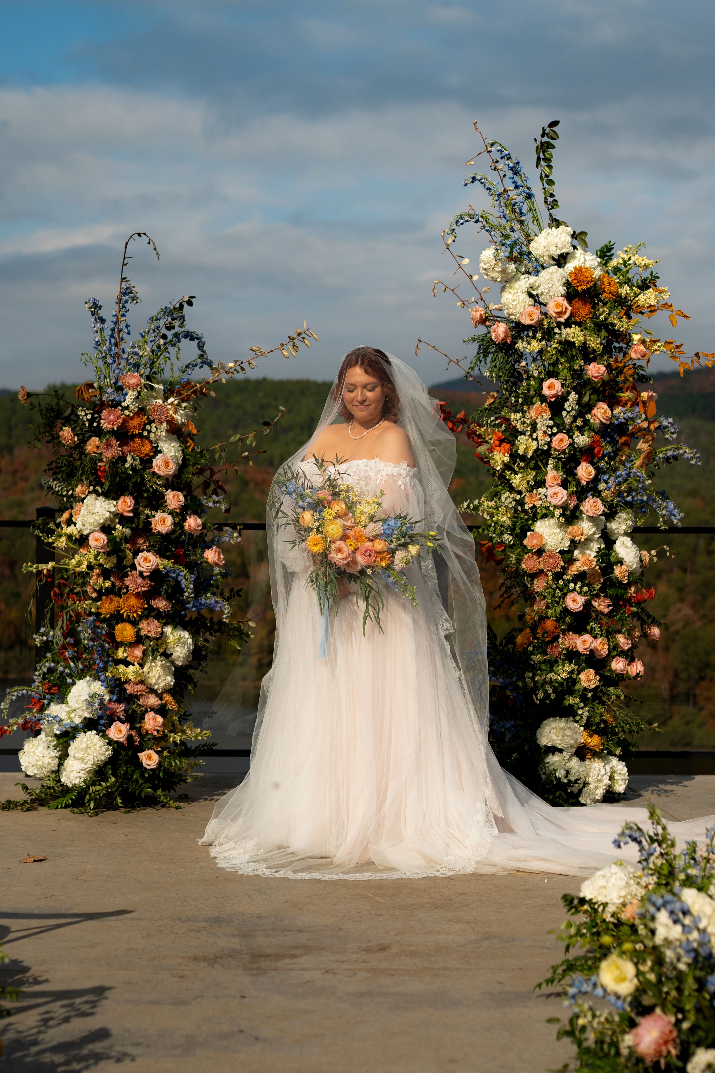 Stunning floral wedding arch with peach and white flowers against a cloudy mountain backdrop.