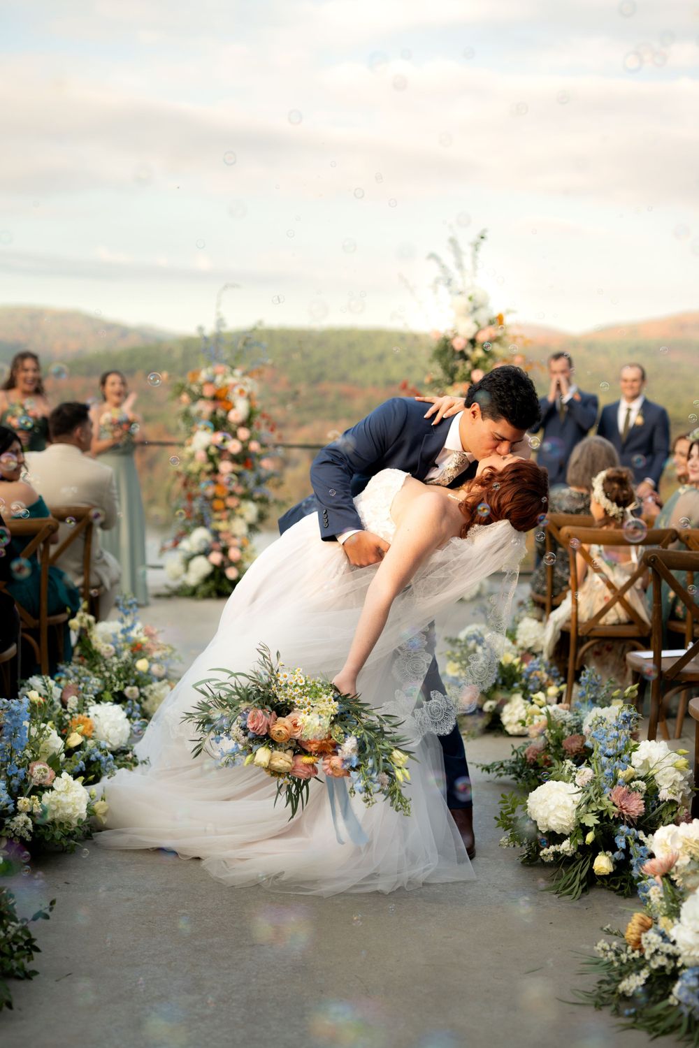 Romantic outdoor wedding moment with lush floral decorations and mountain scenery.