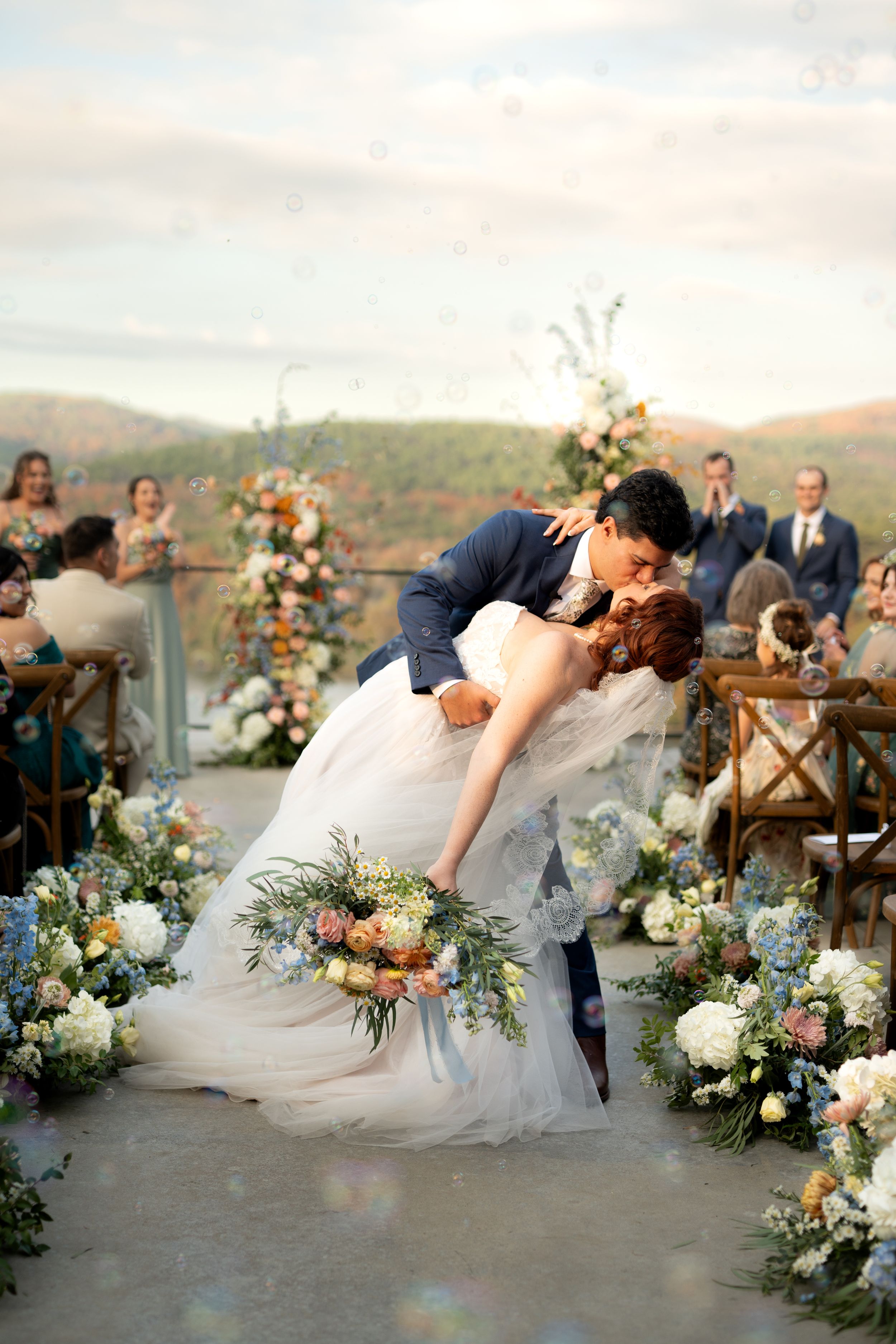 Romantic outdoor wedding moment with lush floral decorations and mountain scenery.